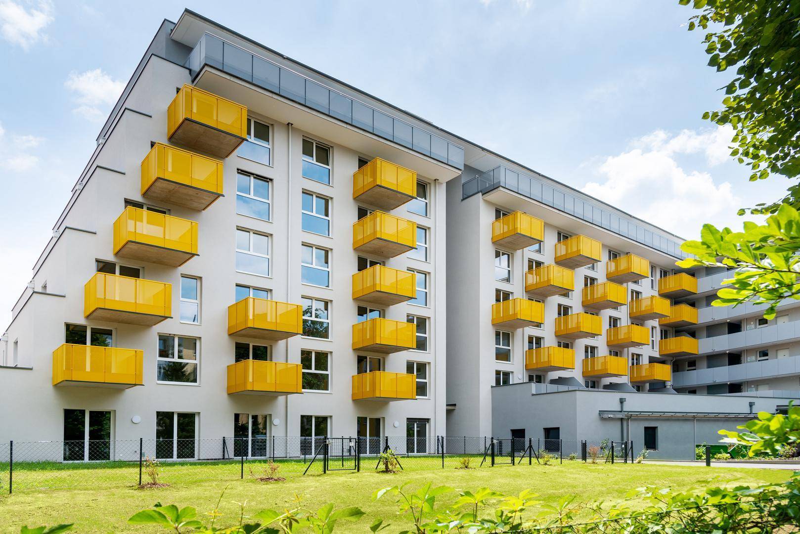 Modernes Mehrfamilienhaus mit auffälligen gelben Balkonen und einer gepflegten Grünfläche.