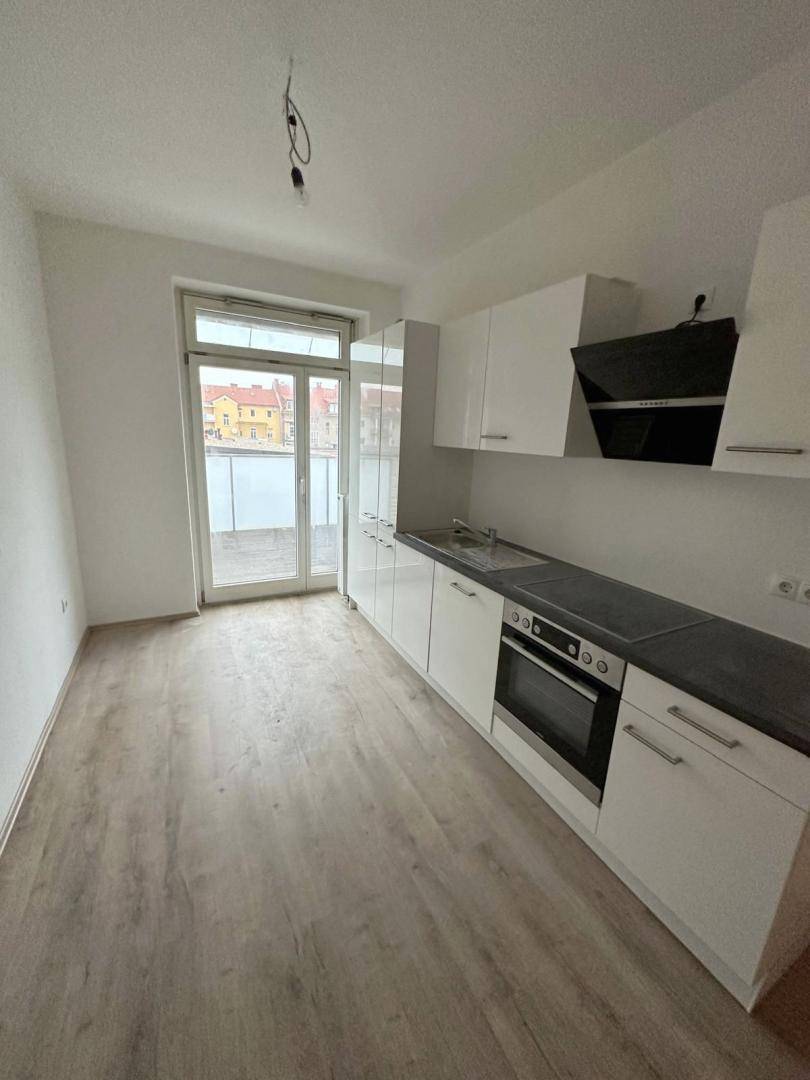 Moderne Küche mit weißen Hochglanzschränken, dunkler Arbeitsplatte und direktem Zugang zum Balkon.