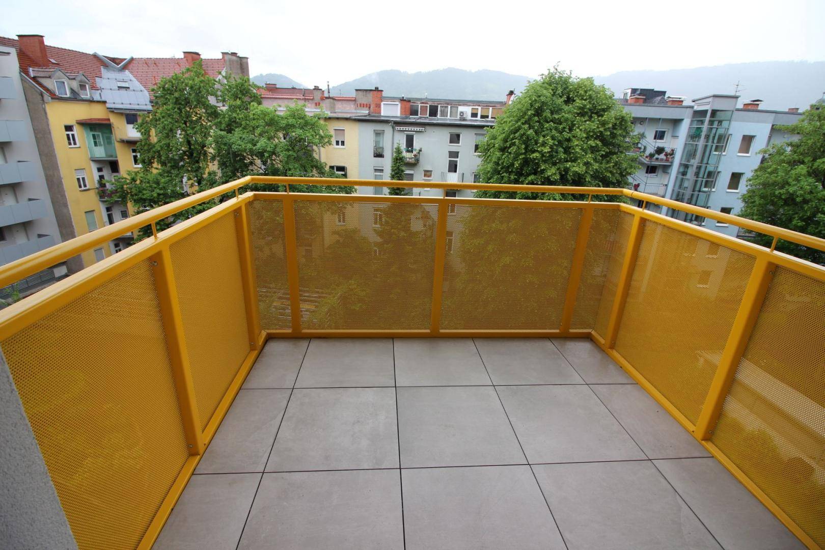 Geräumiger Balkon mit gelbem Geländer und Fliesenboden, bietet einen Blick auf die Stadt.