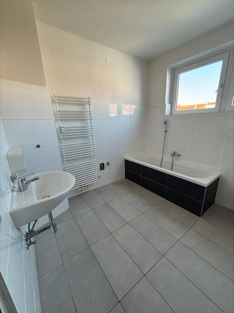 Modernes Badezimmer mit Badewanne, Waschbecken, Fliesenboden und beheiztem Handtuchhalter.