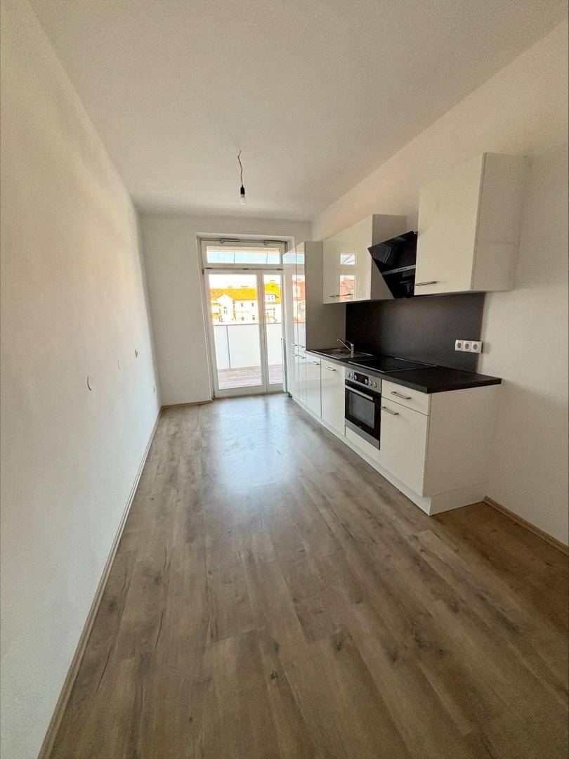 Moderne, kompakte Küche mit weißen Schränken, dunkler Arbeitsplatte und Balkonzugang.