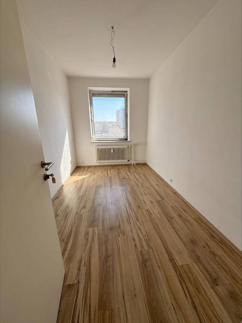 Helles Zimmer mit Holzbalkendecke, Laminatboden und Fenster mit Stadtblick.