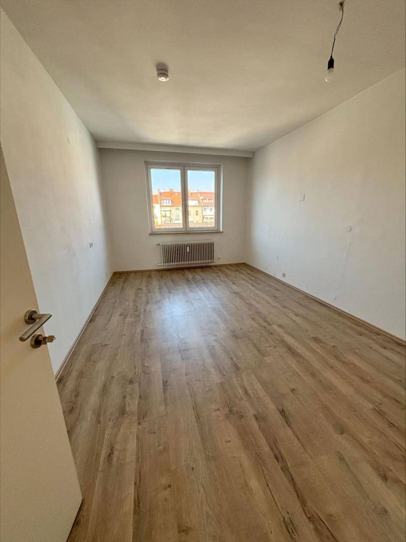 Helles Zimmer mit Laminatboden und Fenster, bietet einen Blick auf die umliegenden Gebäude.