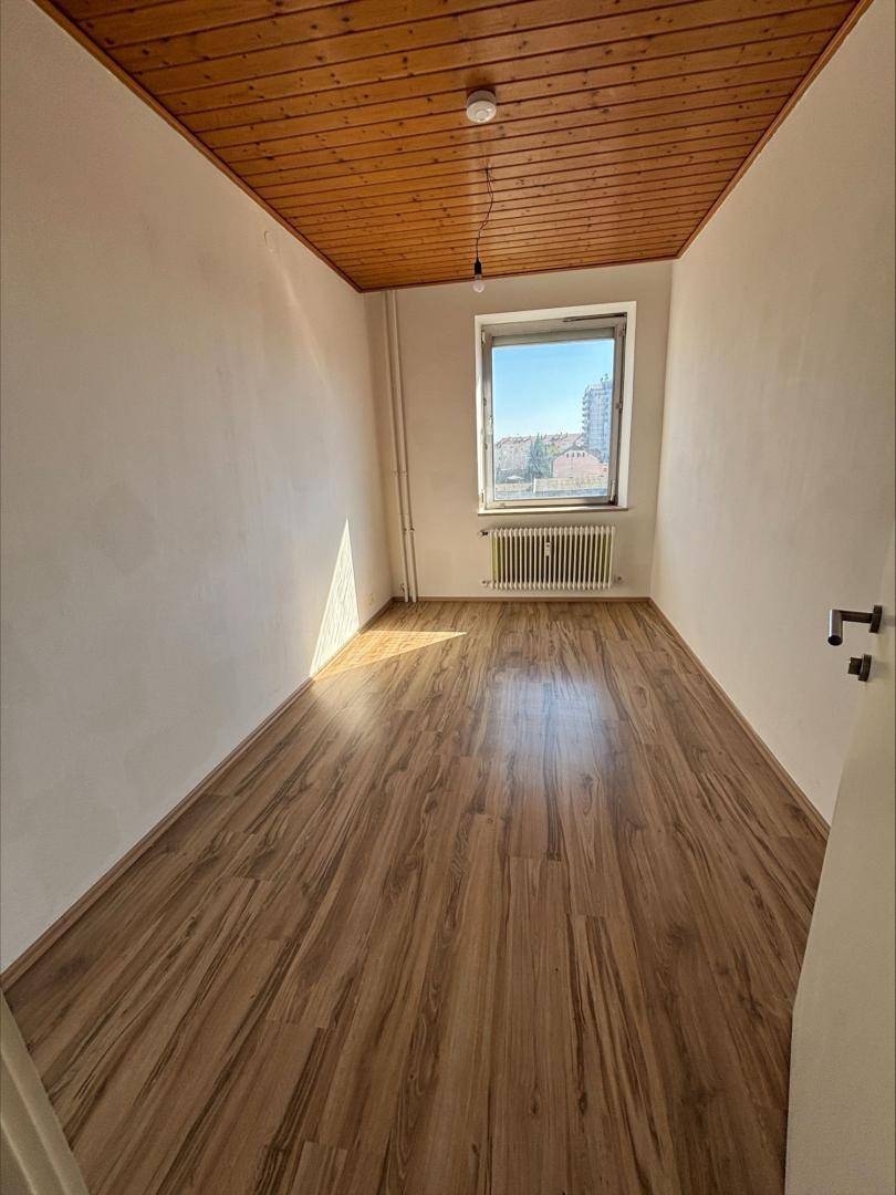 Gemütliches Zimmer mit Holzbalkendecke, Laminatboden und Fenster.
