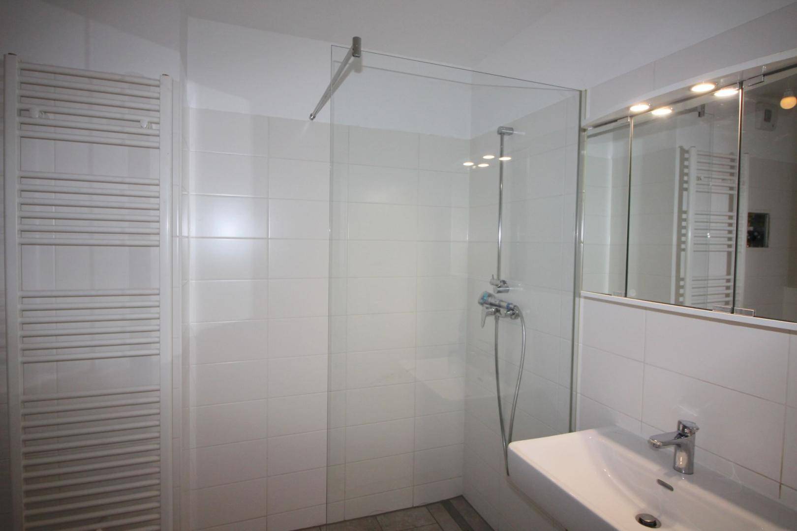 Modernes Badezimmer mit weiß gefliester Dusche, Einzelwaschbecken und beheiztem Handtuchhalter.