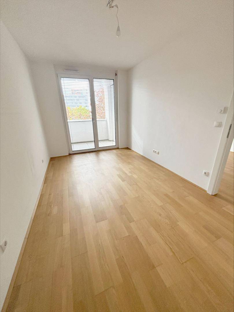 Geräumiges Zimmer mit hellem Parkettboden und Zugang zu einem Balkon, ideal als Schlafzimmer.