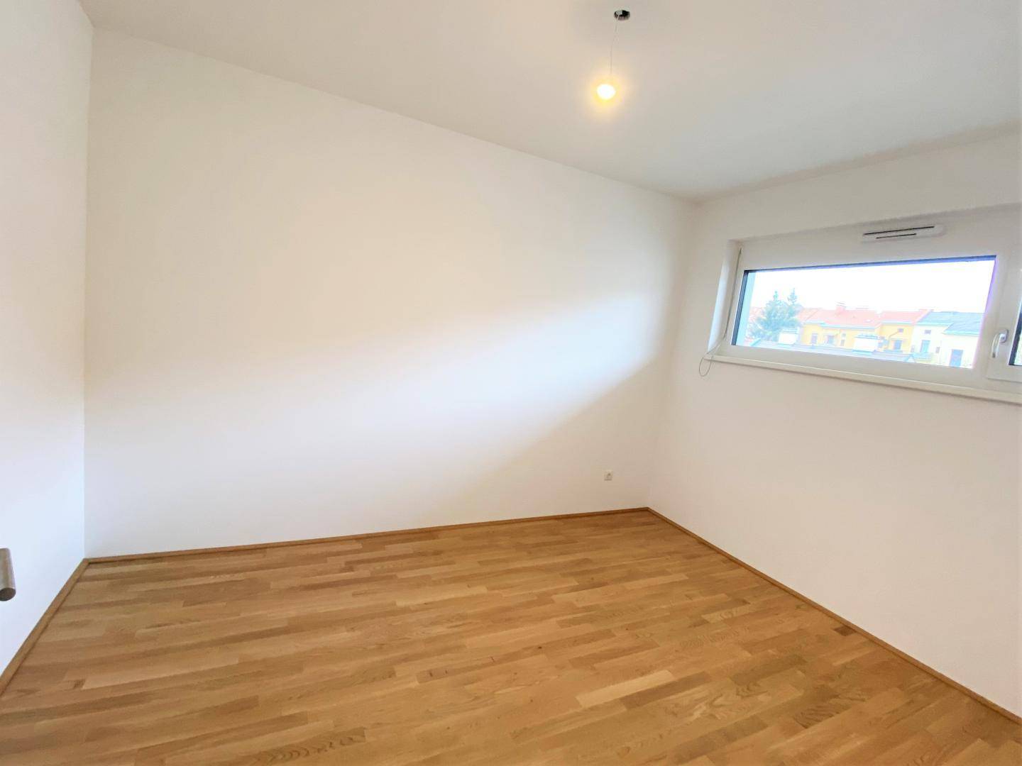 Leeres Zimmer mit Parkettboden und einem Fenster, ideal als Schlaf- oder Arbeitszimmer.