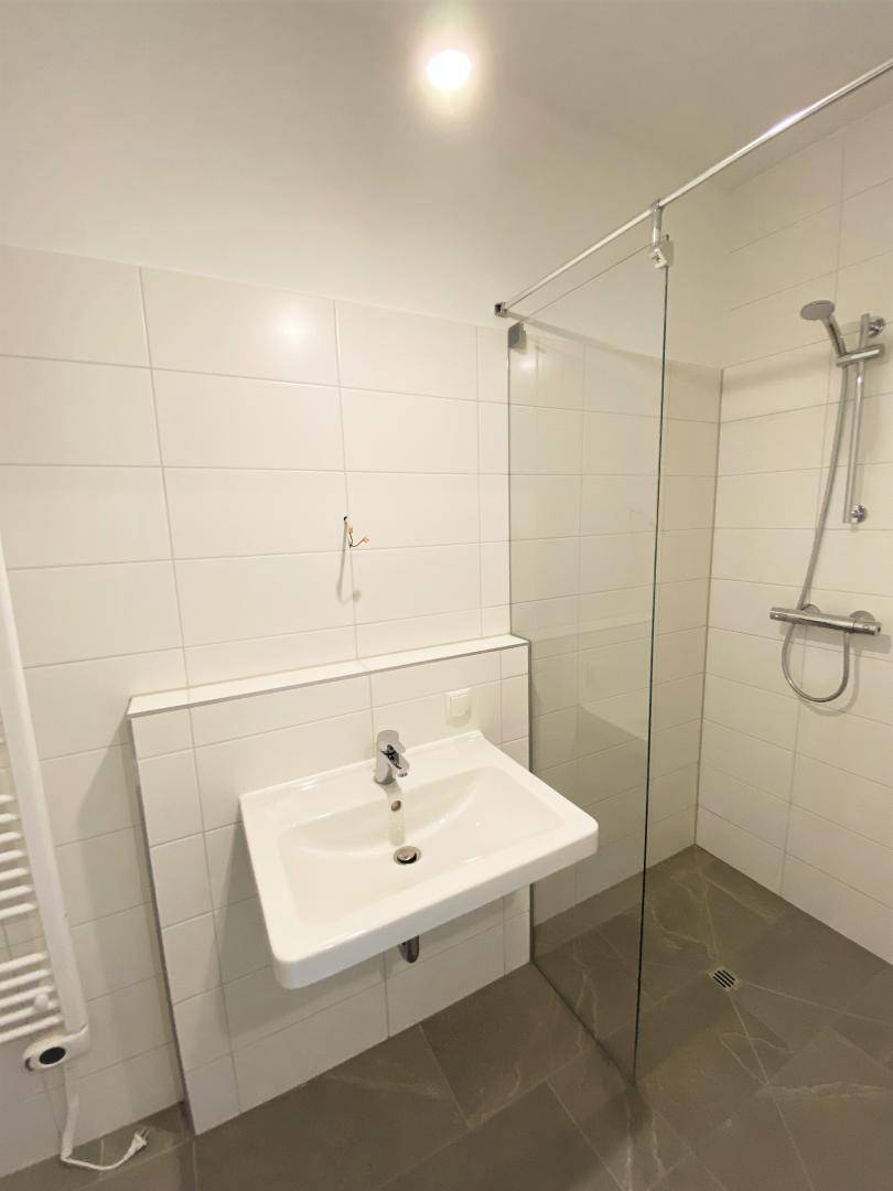 Modernes Badezimmer mit weiß gefliesten Wänden, ebenerdiger Dusche und Einzelwaschbecken.