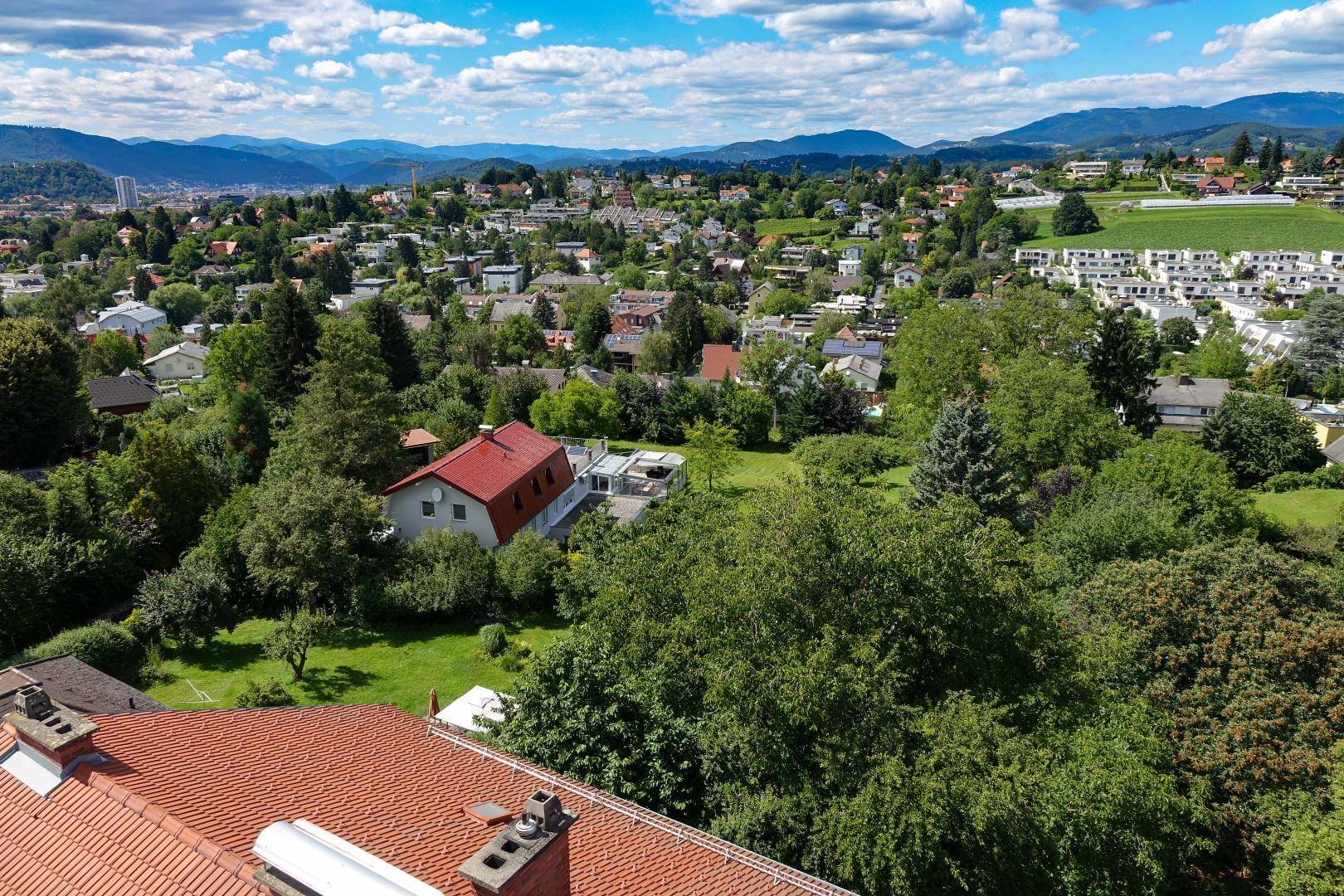 Luftaufnahme einer weitläufigen Wohnsiedlung mit viel Grün und Blick auf die umliegende Hügellandschaft.