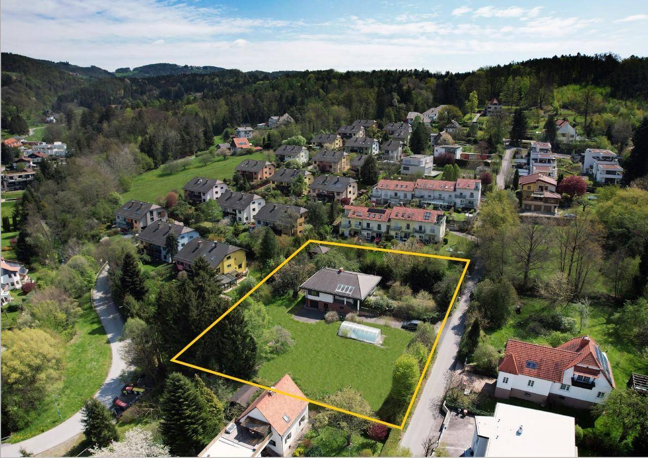 Luftaufnahme eines Hauses mit großem Garten und Pool, umgeben von Wohnbebauung und Natur.