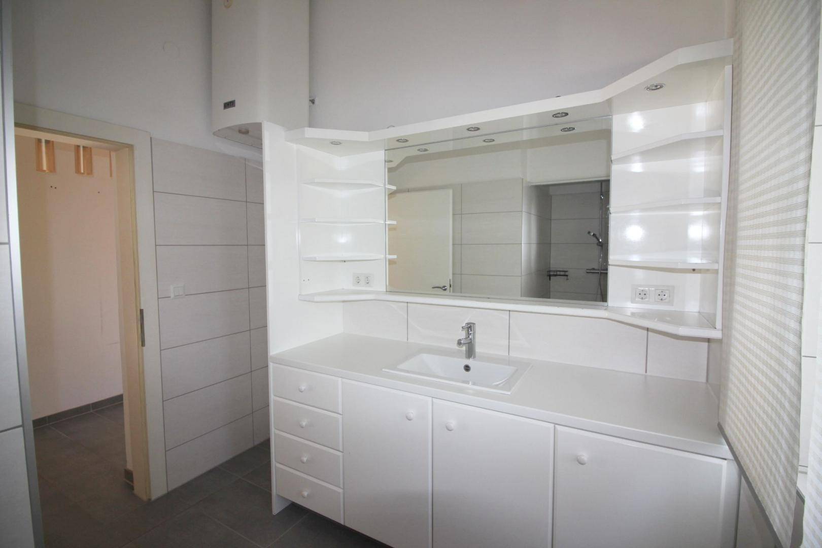Modernes Badezimmer mit weißem Waschtisch, Spiegelschrank und hellen Fliesen.