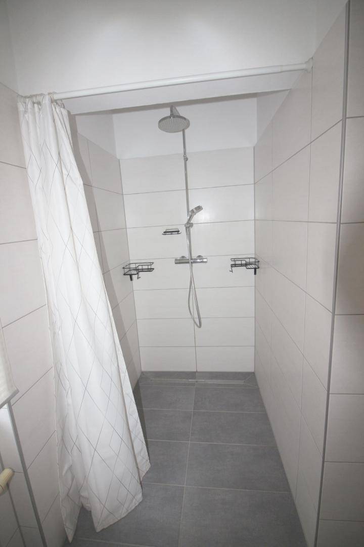 Geräumige Duschkabine mit weißen Fliesen, moderner Regendusche und Handbrause.