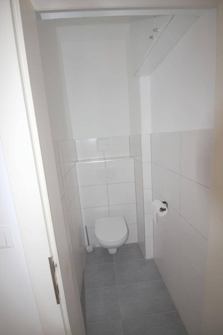 Separates WC mit weißen Fliesen und einer wandmontierten Toilette.