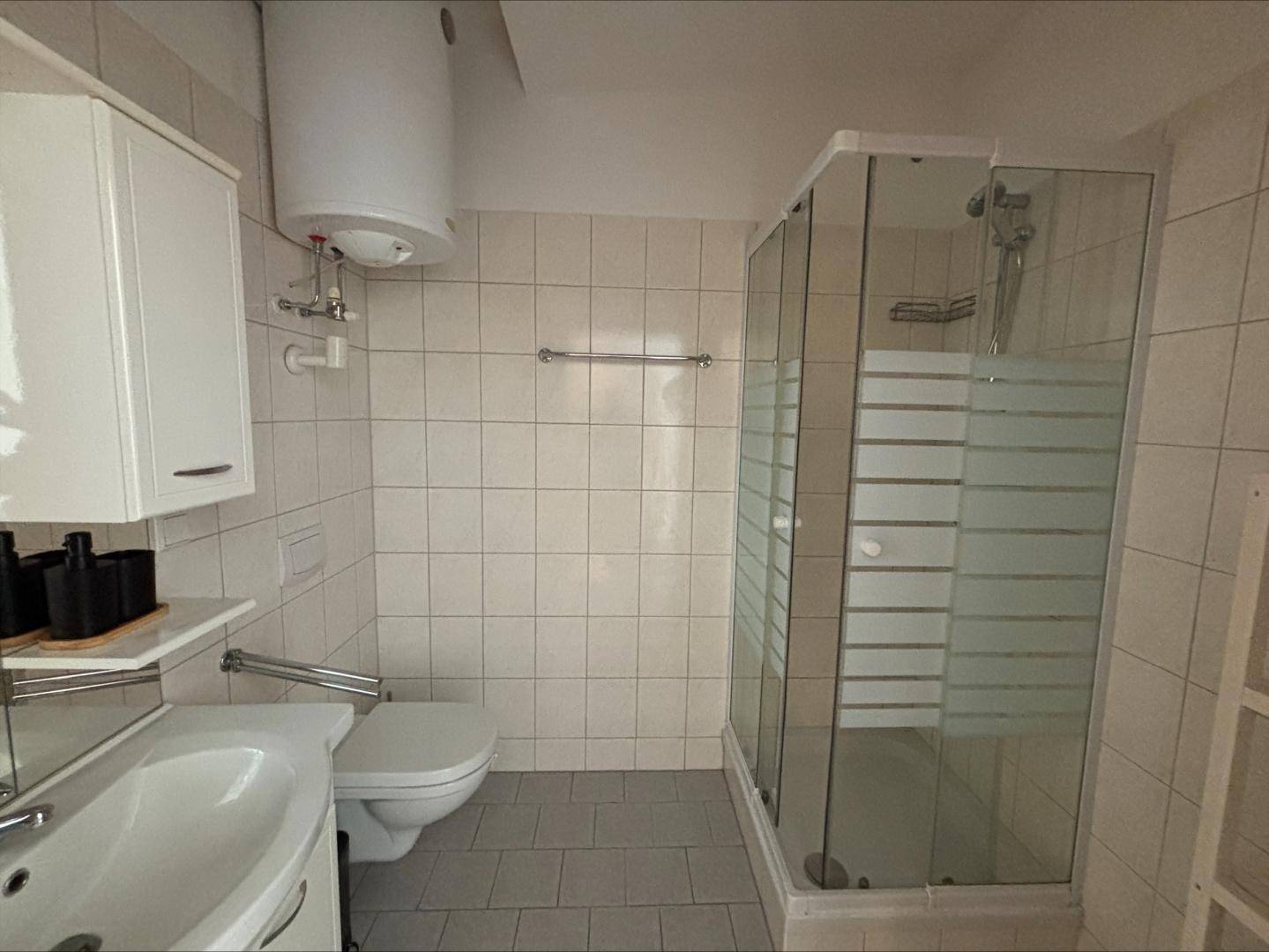 Funktionales Badezimmer mit Dusche, WC, Waschbecken und hellen Fliesen.