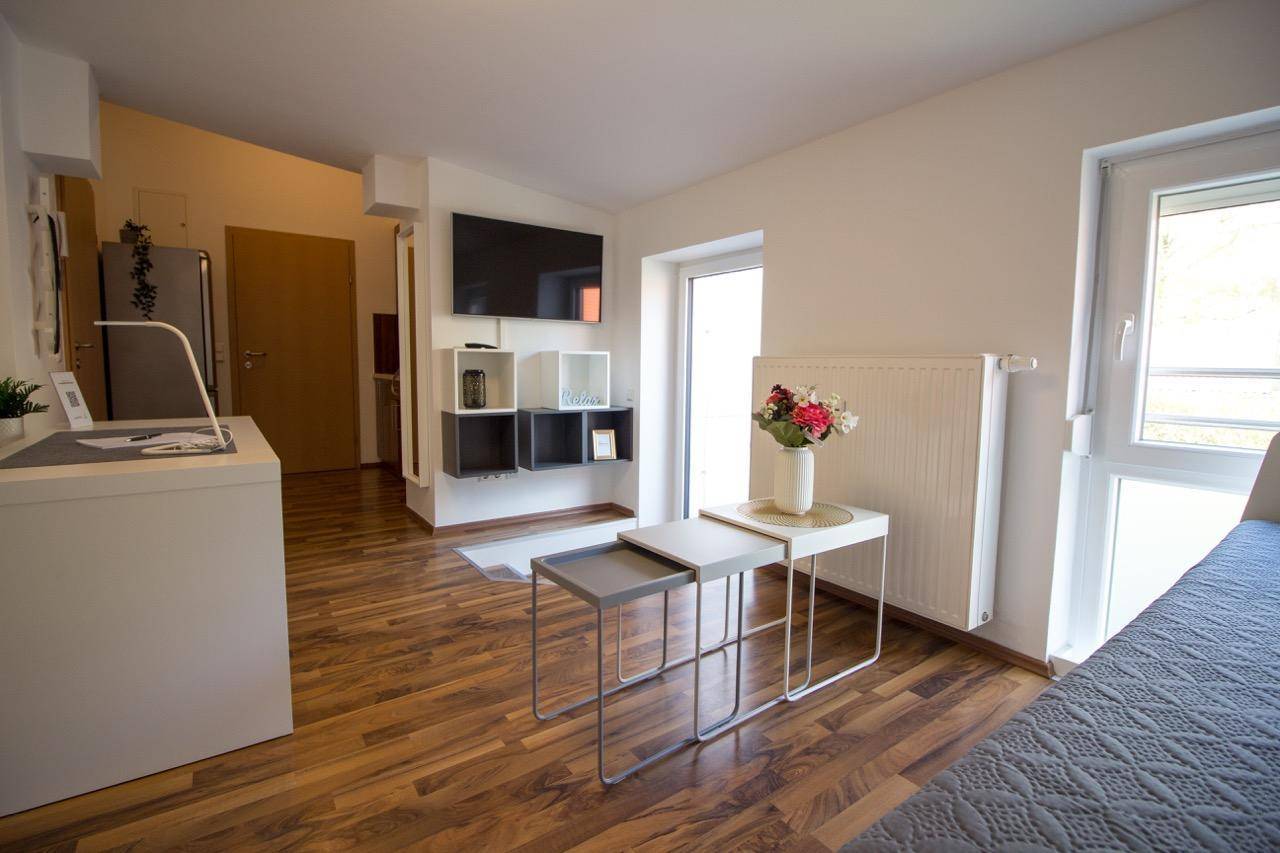 Heller Wohnbereich mit Zugang zum Balkon, Holzboden und einem Wandfernseher.