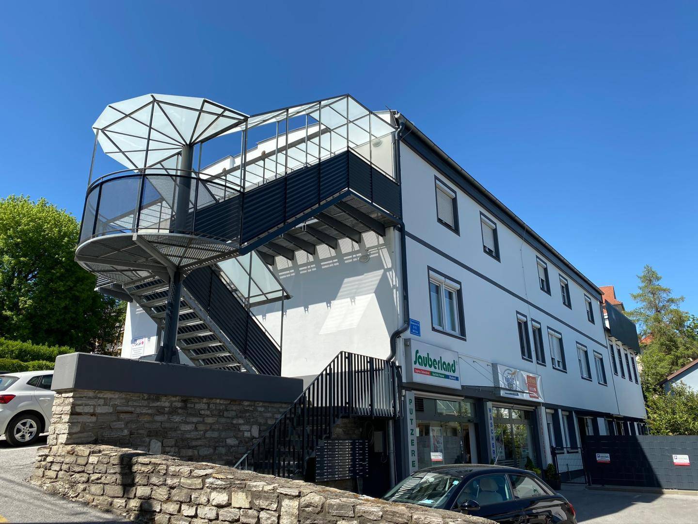 Mehrfamilienhaus mit moderner Fassade, Außentreppe und Geschäften im Erdgeschoss.