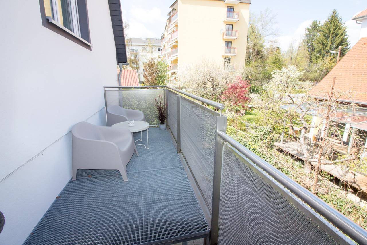 Kleiner Balkon mit Metallboden und zwei Stühlen, bietet Blick auf grüne Umgebung.