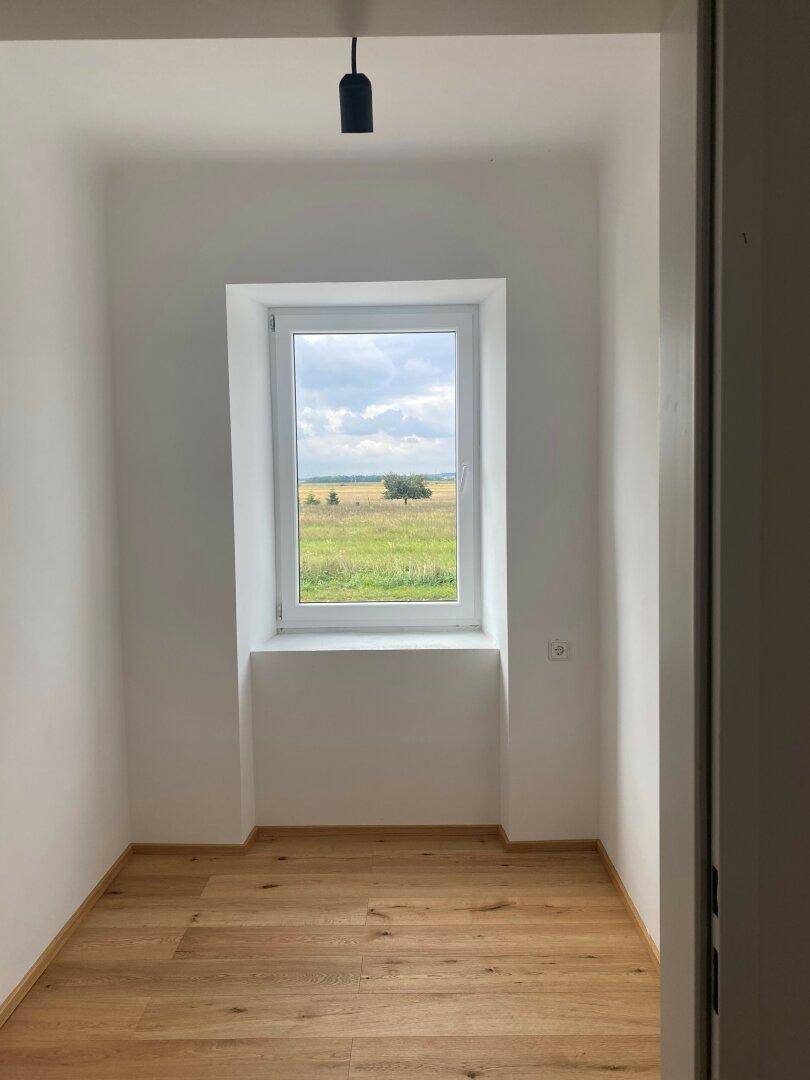 Schmaler Raum mit Holzboden und Fenster, das einen weiten Blick ins Grüne bietet.