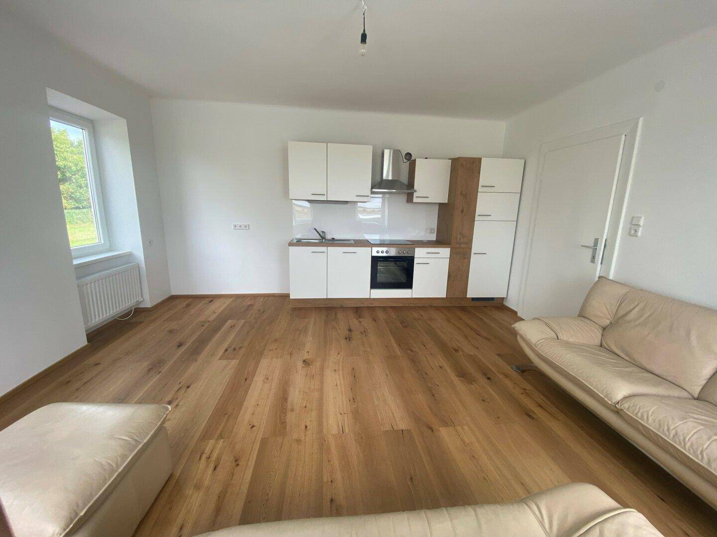 Heller Wohnbereich mit Holzboden und einer modernen Küchenzeile in Weiß und Holzoptik.