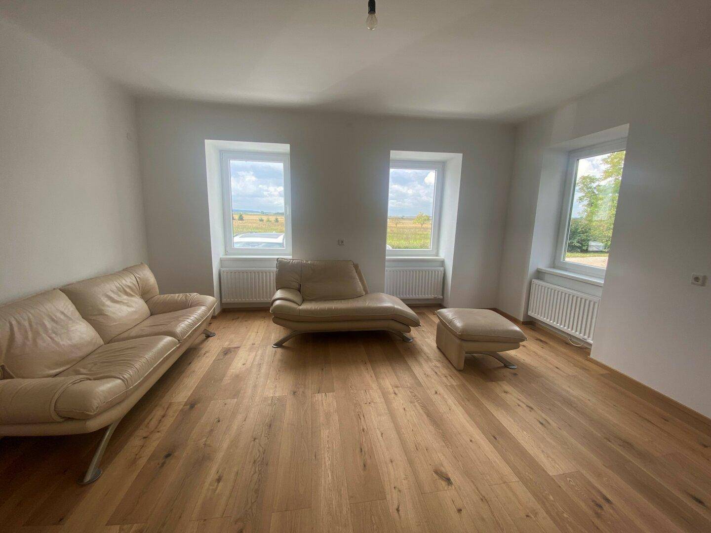 Helles Wohnzimmer mit Holzboden, beigen Möbeln und weitem Blick ins Grüne.