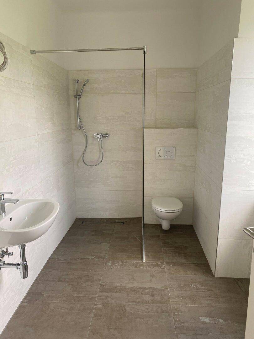 Modernes Badezimmer mit ebenerdiger Dusche, Wand-WC und hellen großformatigen Fliesen.