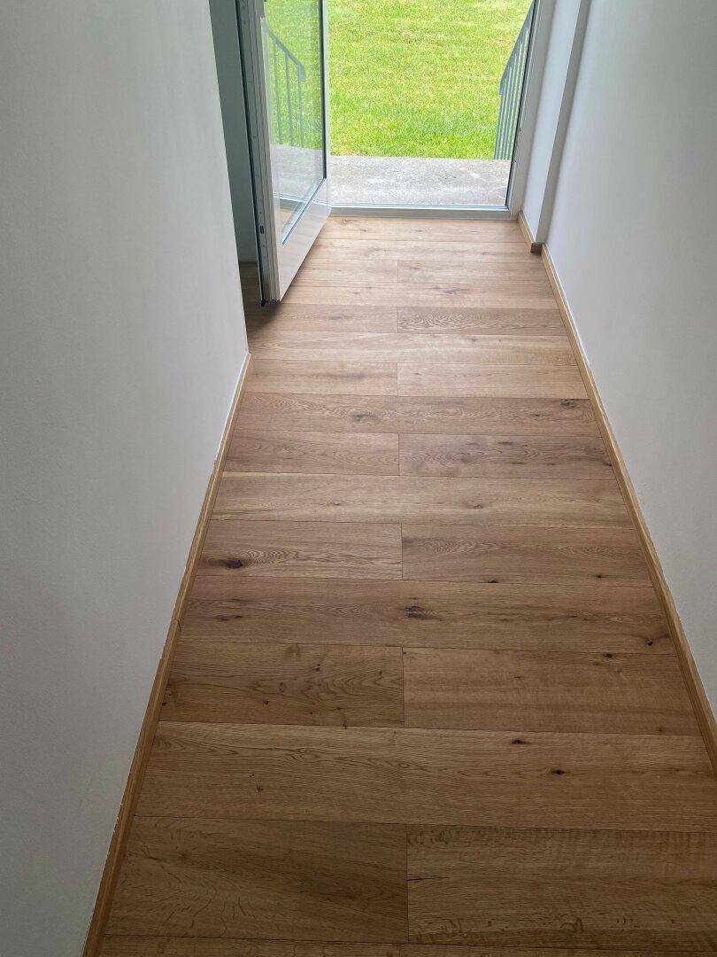 Heller Flur mit Holzboden und offenem Zugang zu einem Außenbereich mit Rasenfläche.
