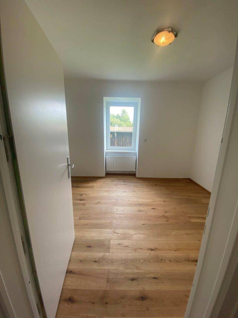 Leeres Zimmer mit Holzboden und Fenster, ideal als Schlaf- oder Arbeitszimmer mit Blick ins Grüne.