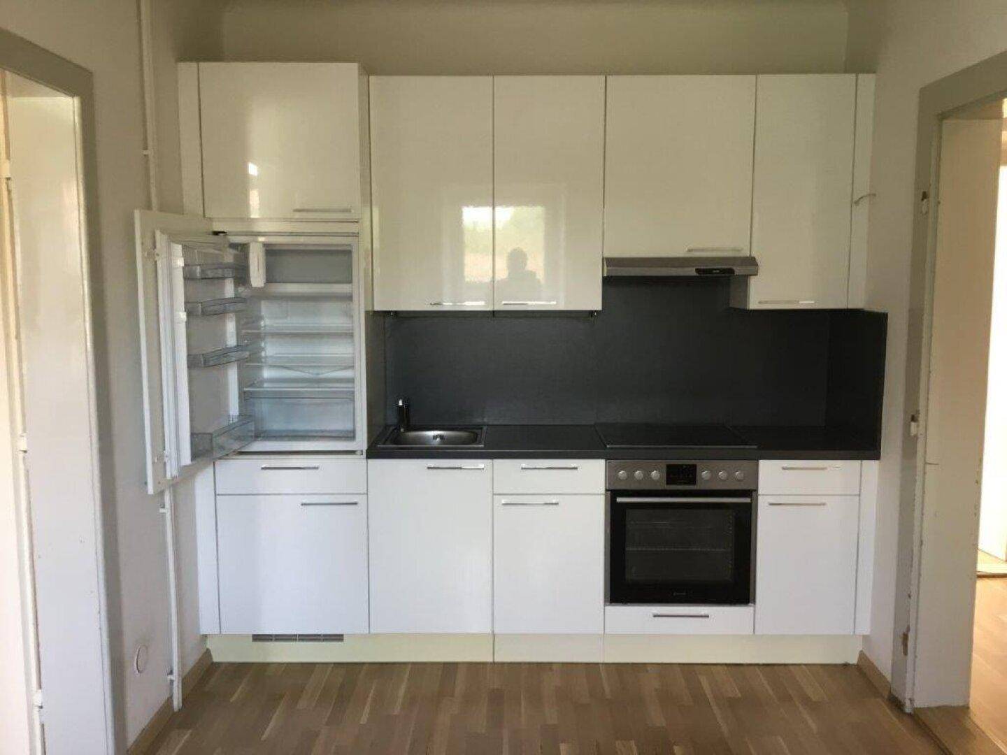 Kleine, moderne Küche mit weißen Hochglanzfronten und integriertem Kühlschrank und Backofen.