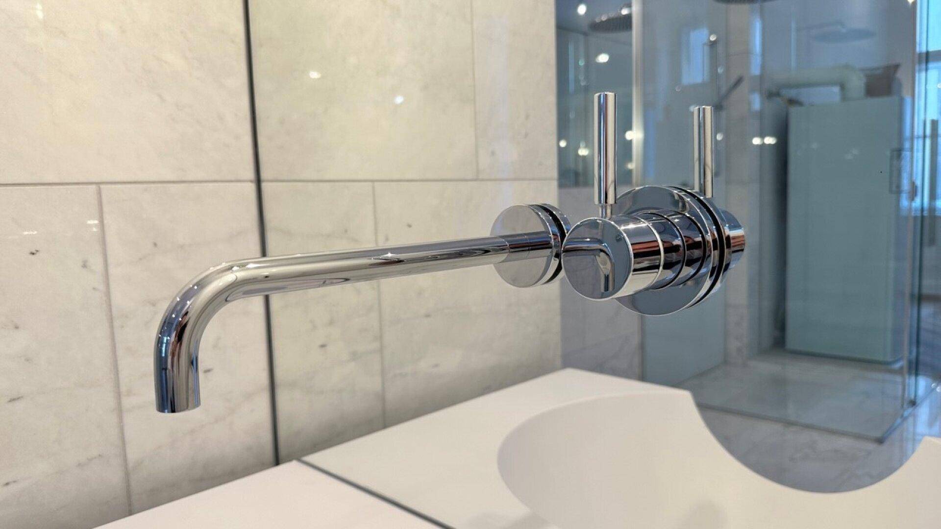 Detailansicht eines modernen Wandwasserhahns mit glänzender Chromoberfläche im Badezimmer.