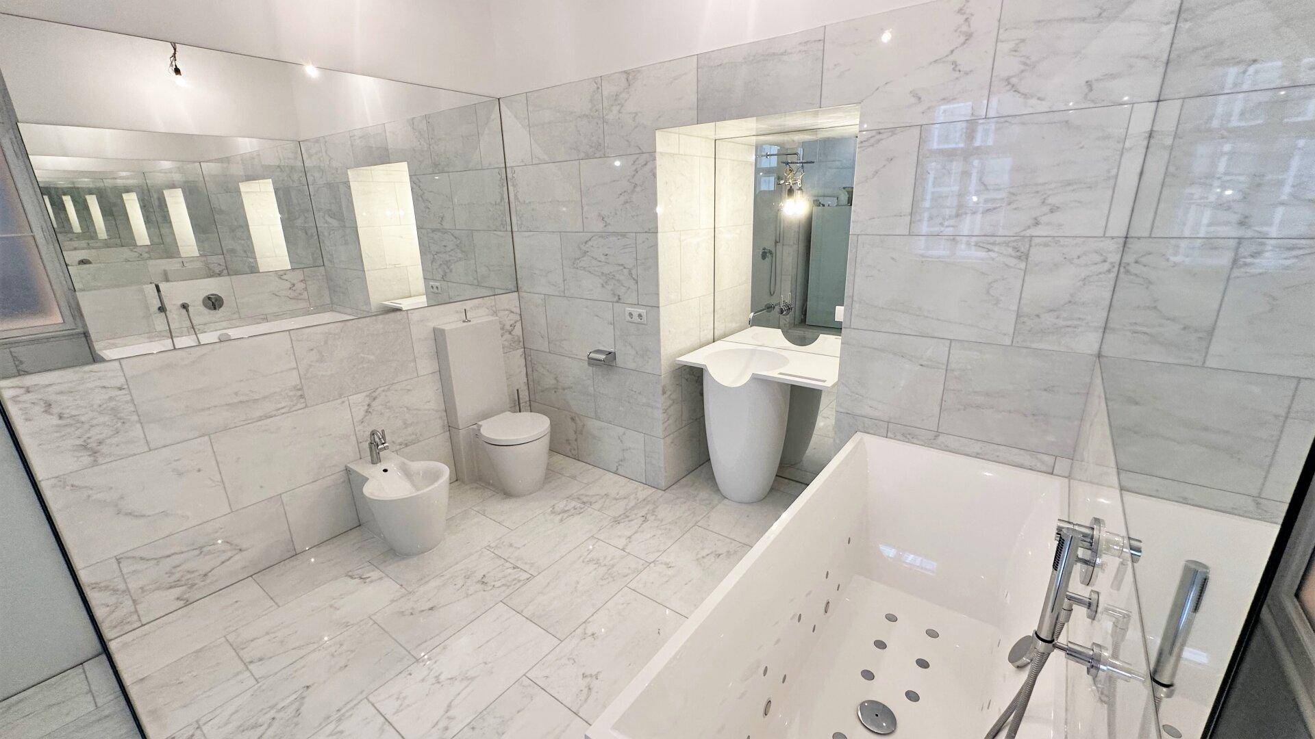 Luxuriöses Badezimmer mit Marmorfliesen, Badewanne, Bidet und modernem Waschtisch.