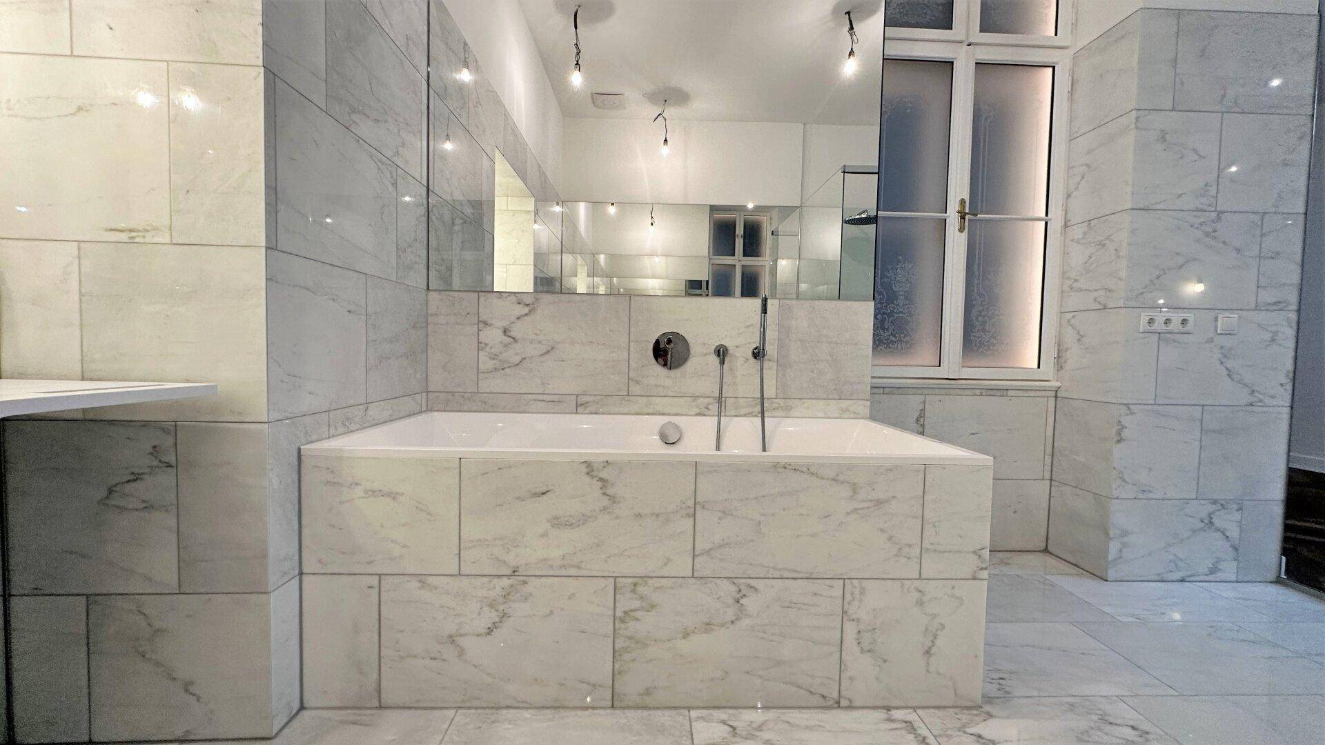 Elegantes Badezimmer mit Marmorfliesen und einer eingebauten Badewanne unter einem großen Spiegel.