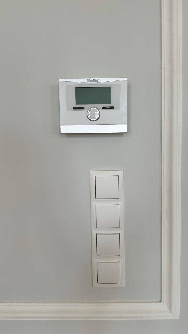 Moderner Thermostat und Lichtschalter an einer eleganten Wand mit Zierleisten.