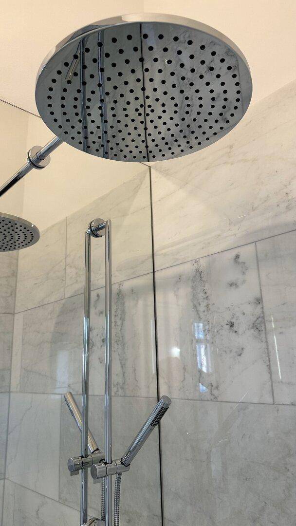 Detailansicht einer großen Regendusche mit Chromarmaturen in einem modernen Badezimmer.