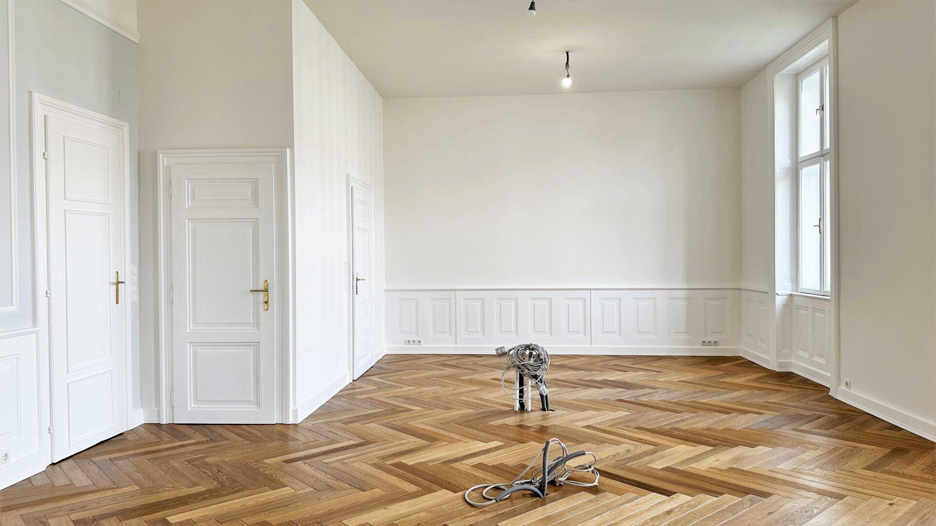 Heller Raum mit Fischgrätparkett, hohen Decken und klassischen weißen Türen.