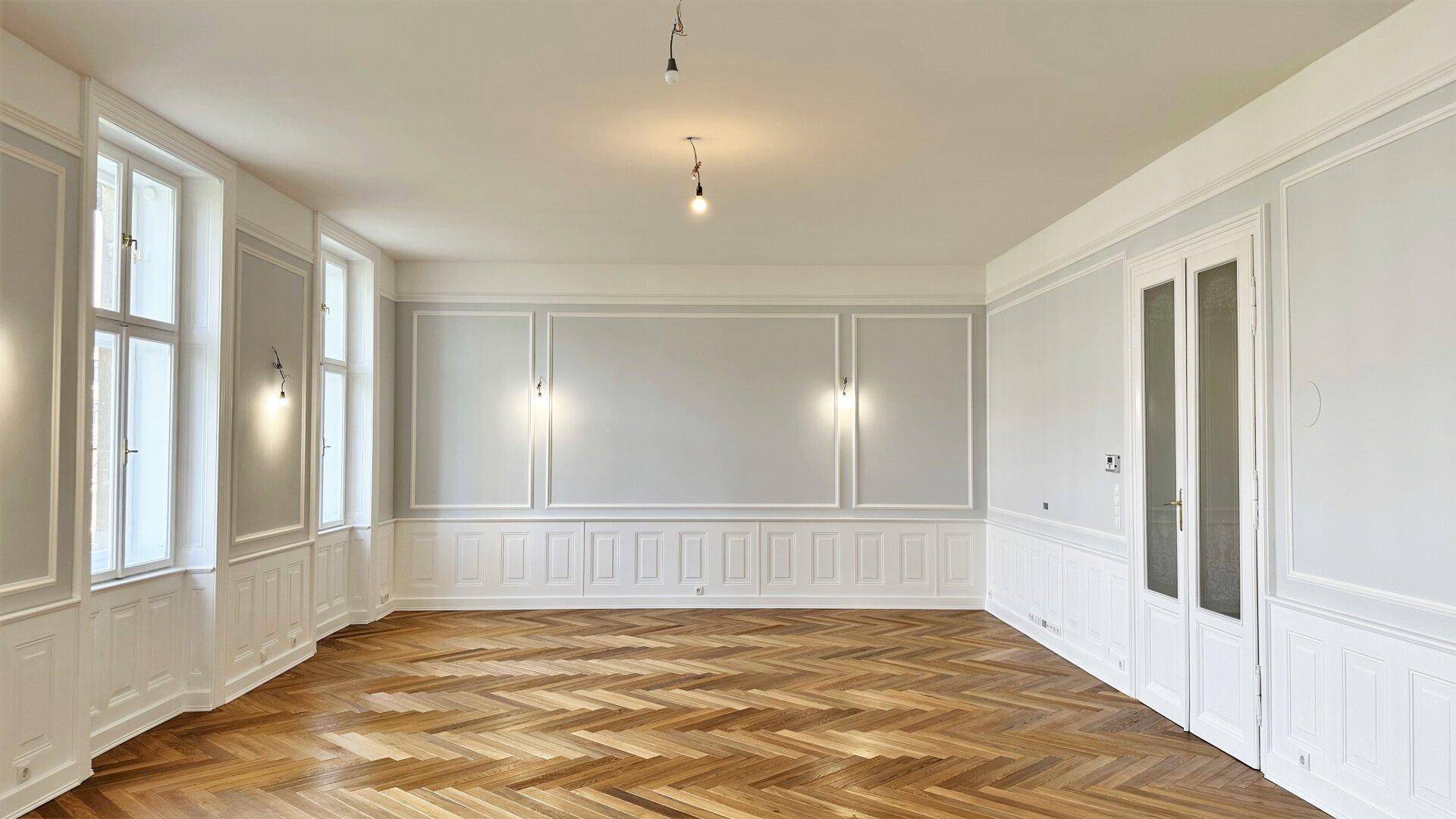 Geräumiges Wohnzimmer mit klassischer Wandvertäfelung, Fischgrätparkett und hohen Decken.
