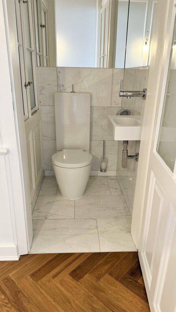Kleines Gäste-WC mit Marmorfliesen, wandhängender Toilette und modernem Waschbecken.