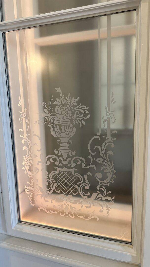 Detailaufnahme eines satinierten Glasfensters mit kunstvollen floralen Mustern.