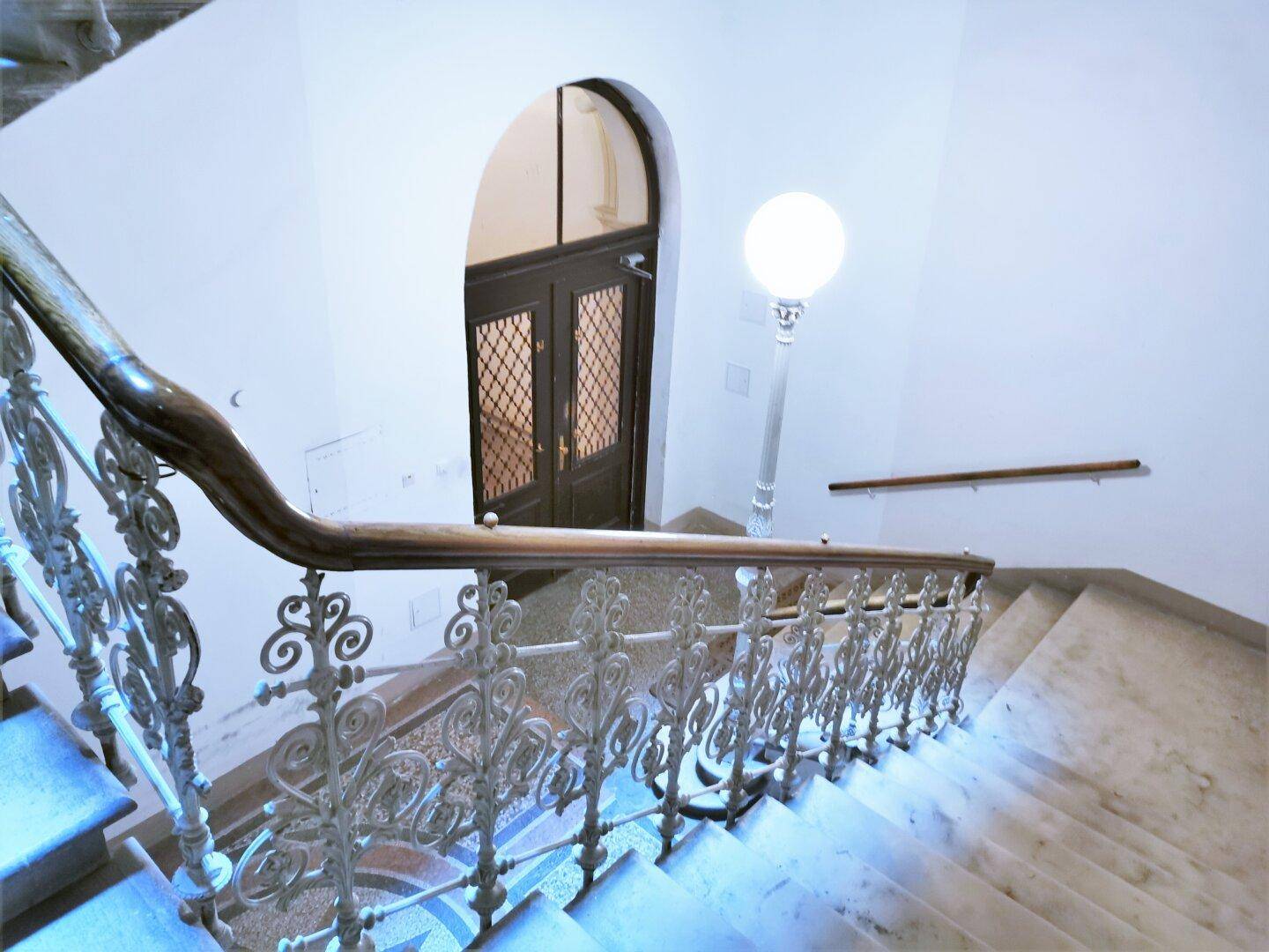 Historisches Treppenhaus mit schmiedeeisernem Geländer und einer eleganten Bogen-Eingangstür.