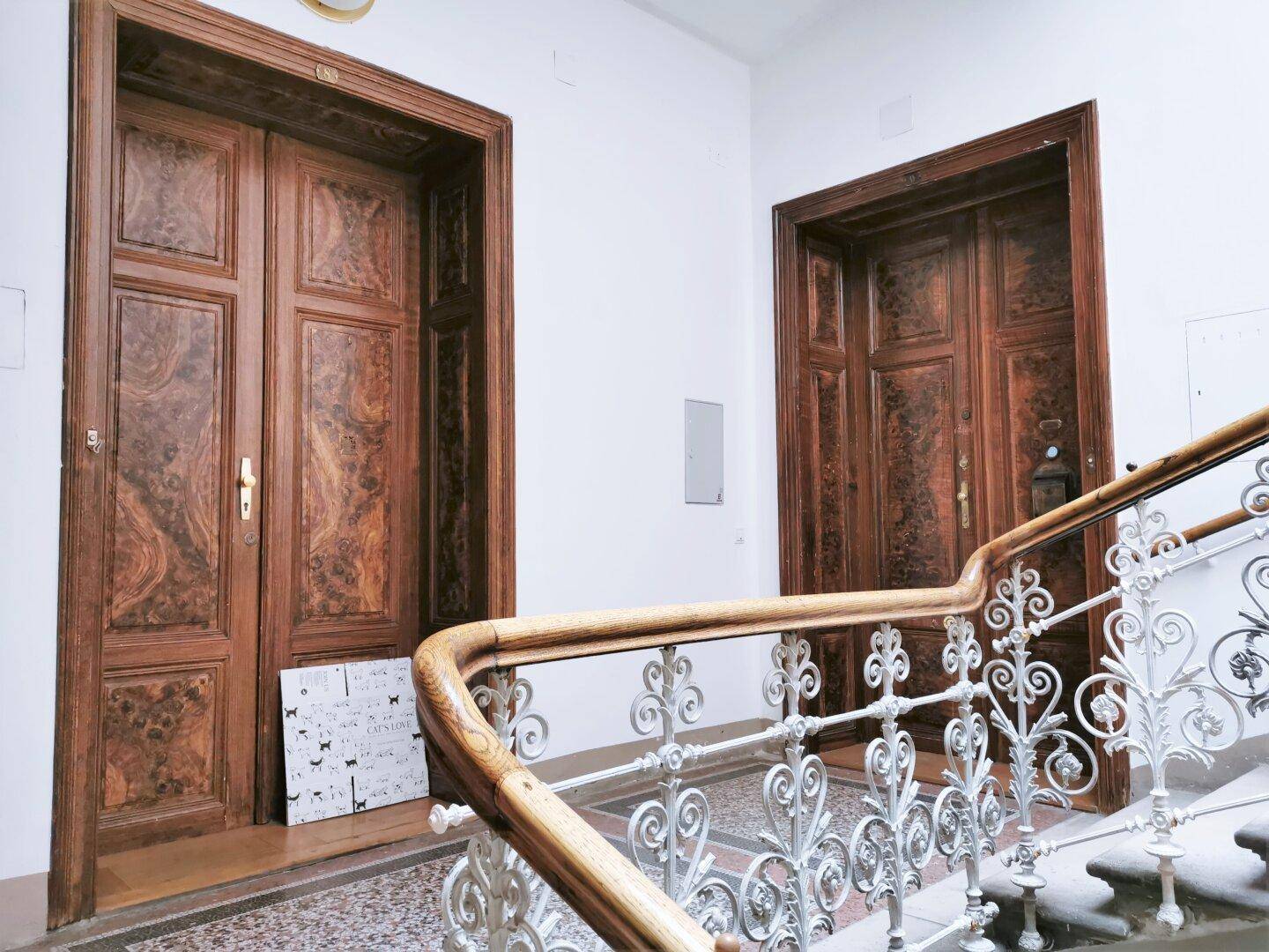Elegantes Treppenhaus mit kunstvollem Geländer und zwei großen Holztüren im klassischen Stil.