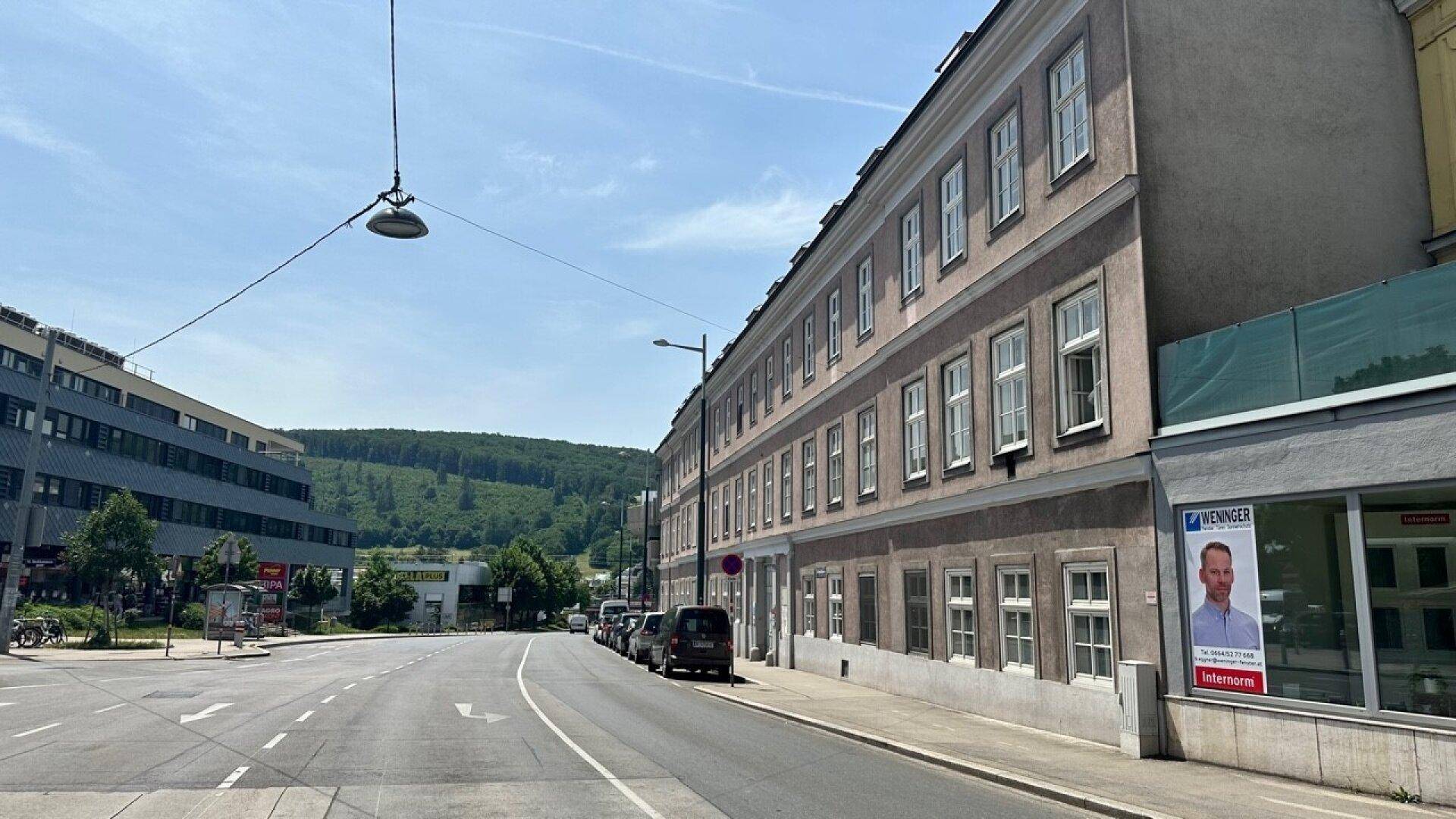 Ansicht eines Altbaus mit Mansarddach und Geschäften im Erdgeschoss an einer Straße.