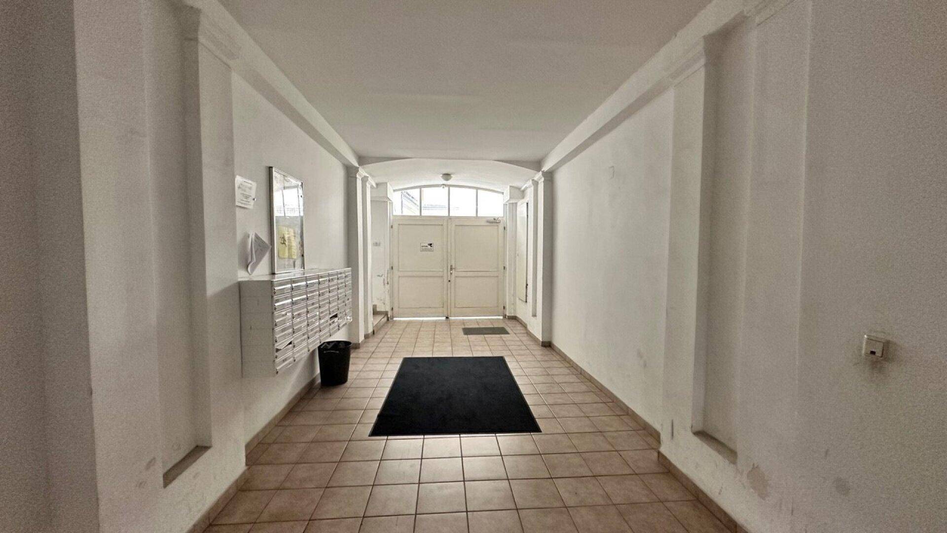 Heller Eingangsbereich mit Fliesenboden, Briefkästen und Doppeltüren zum Innenhof.