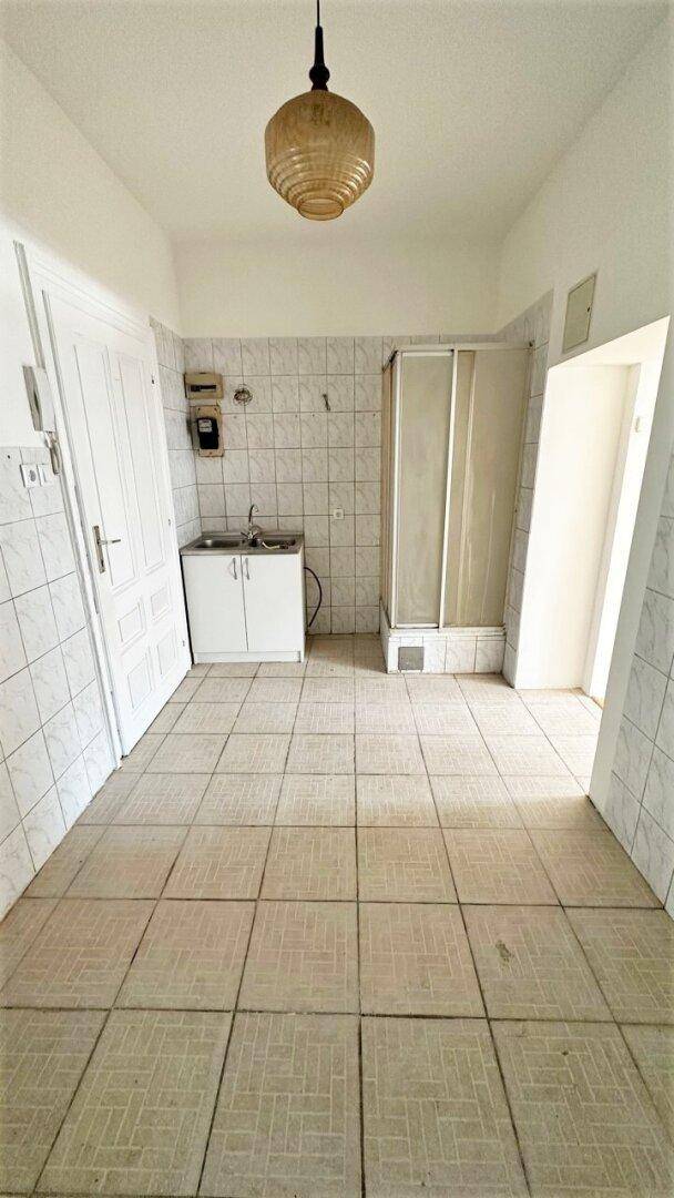 Einfaches Badezimmer mit Fliesenboden, Duschkabine und Waschbeckenunterschrank.