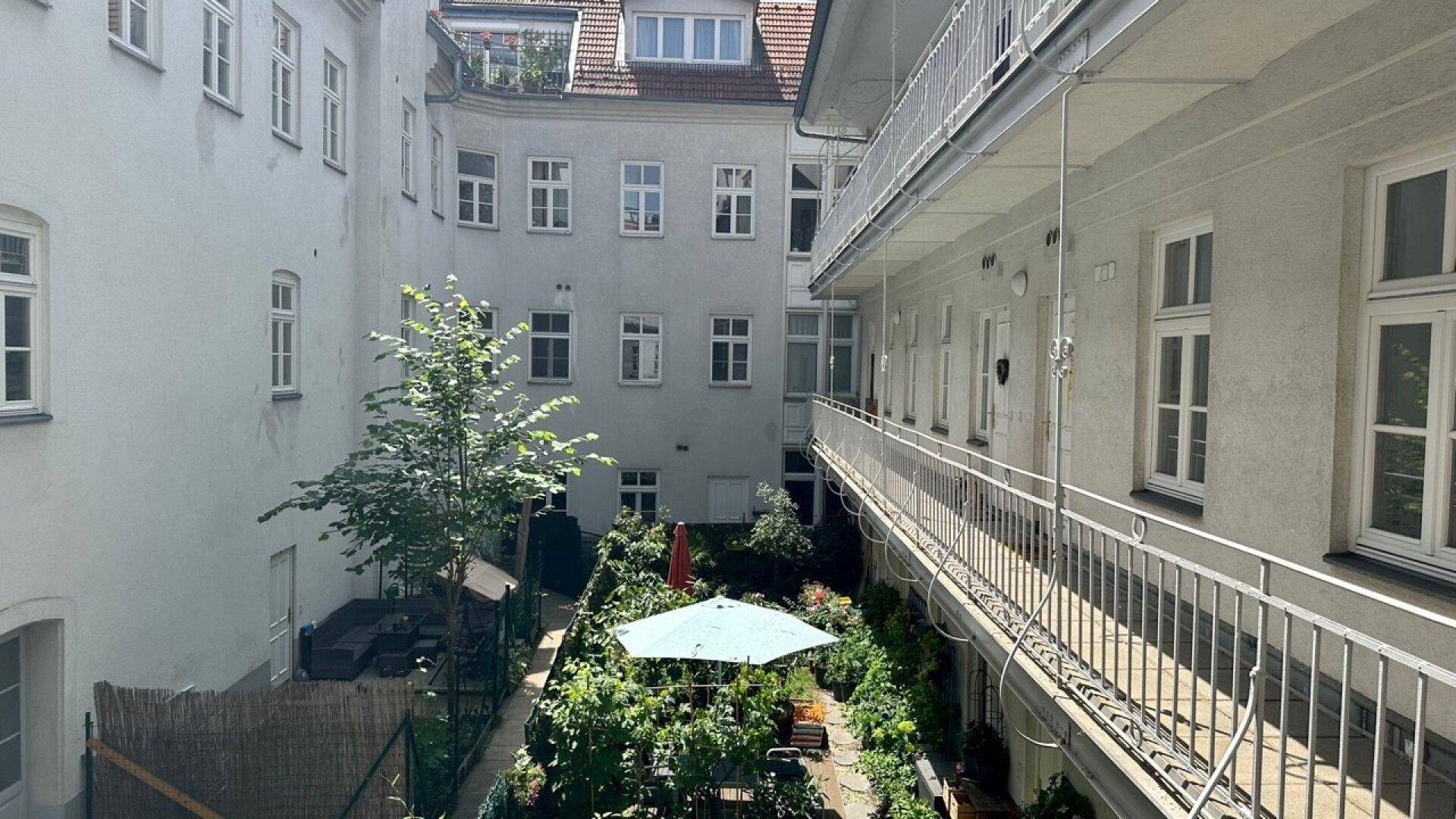 Grüner Innenhof mit üppiger Vegetation, Sitzgelegenheiten und umlaufenden Balkonen.