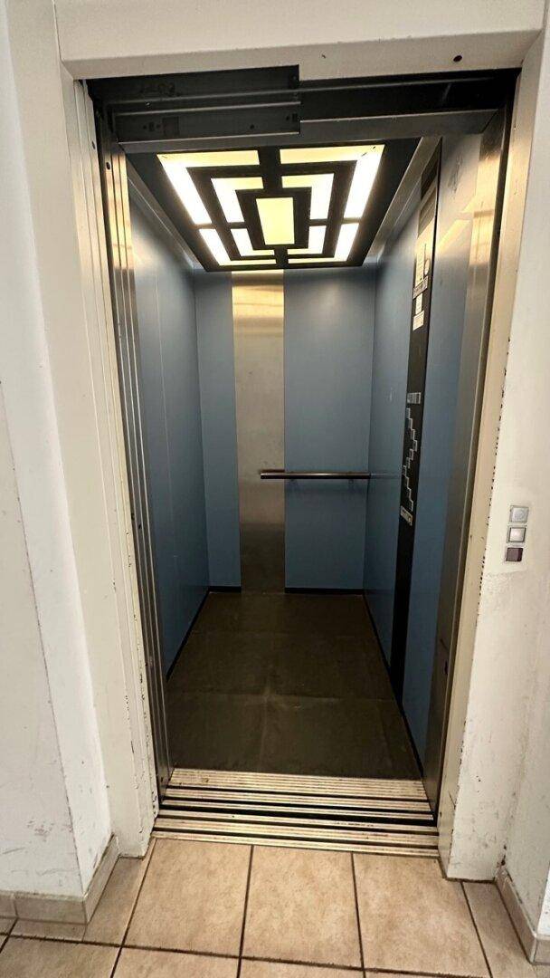 Moderner Aufzug mit Edelstahloberflächen und einer stilvollen Deckenbeleuchtung.