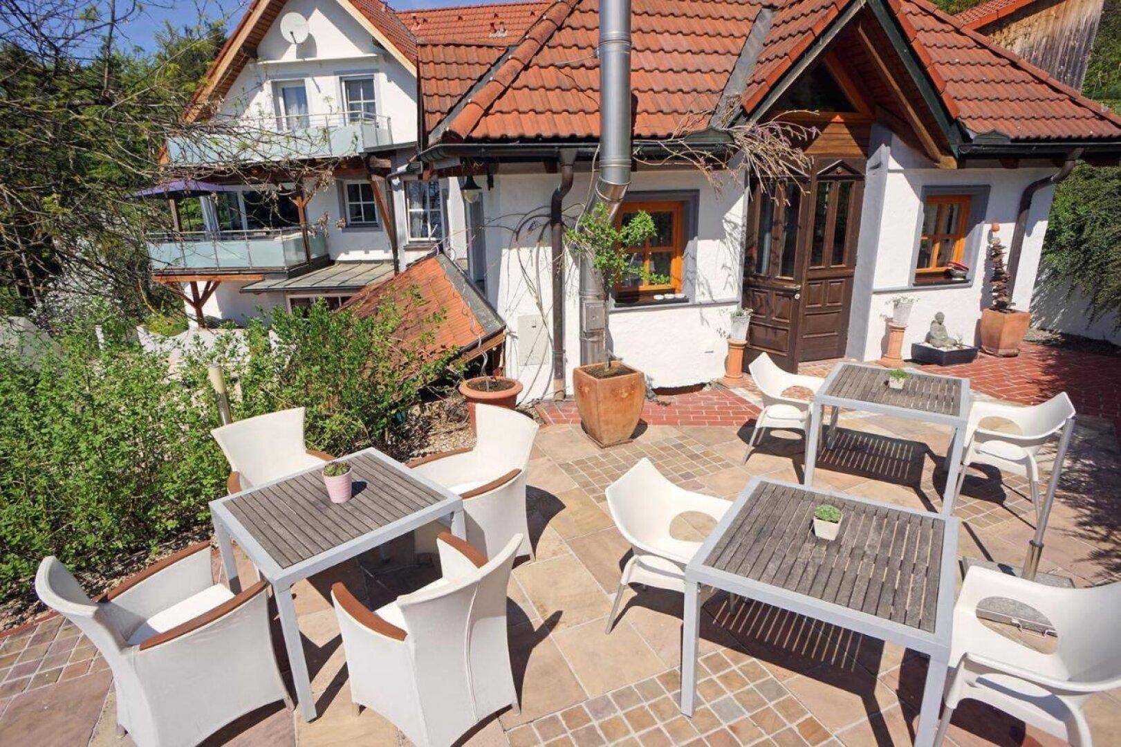 Gemütliche Außenterrasse mit Tischen und Stühlen, ideal für Mahlzeiten im Freien, neben dem Gebäude.
