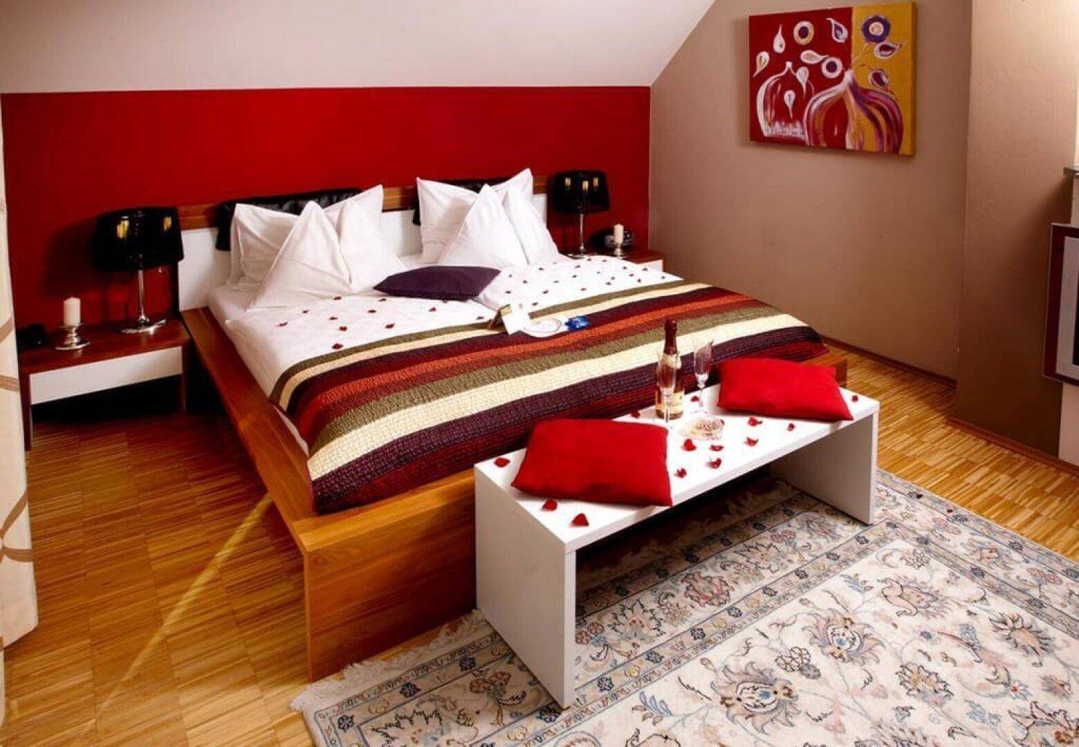 Helles Schlafzimmer mit Holzboden, roter Akzentwand und einem Teppich, dekoriert mit Rosenblättern.