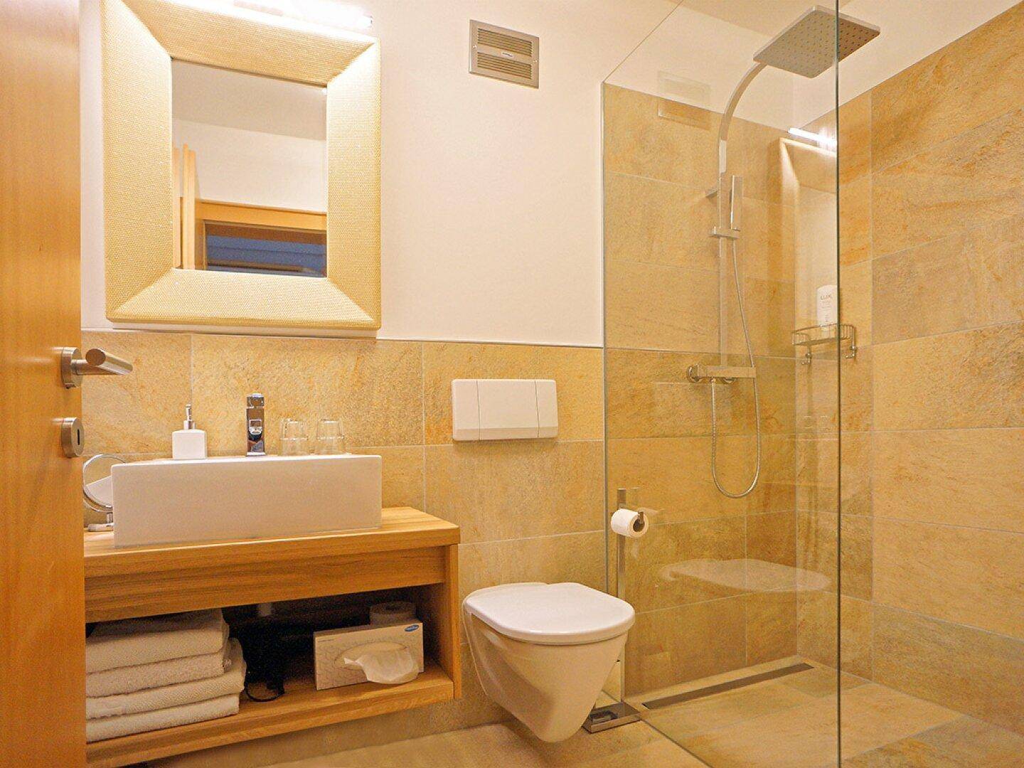 Modernes Badezimmer mit begehbarer Dusche, wandhängendem WC und Natursteinfliesen.