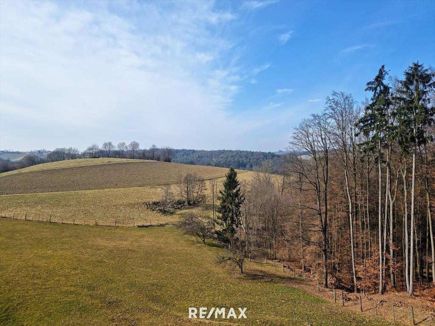 Panoramablick über hügelige Felder und Wälder unter einem weiten blauen Himmel.