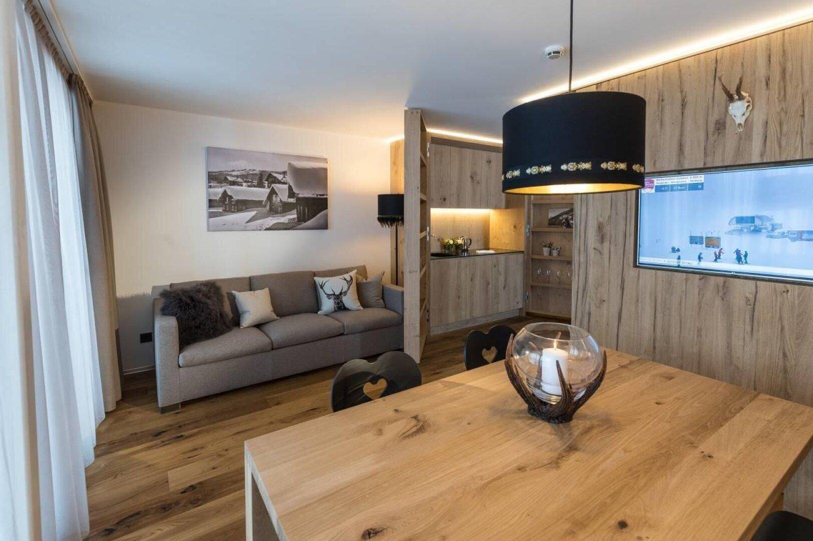 Gemütlicher Wohn-Essbereich mit Holztisch, Sofa und integrierter Küchenzeile im alpinen Stil.