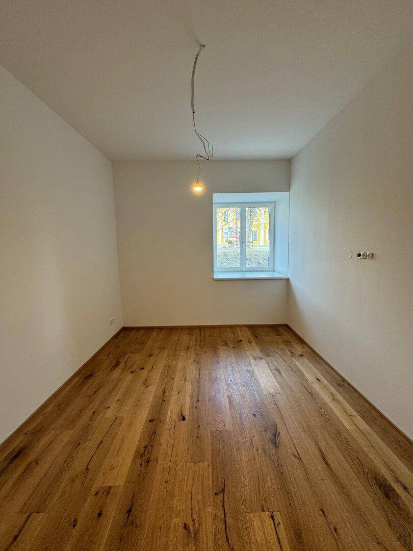 Helles Schlafzimmer mit Holzdielenboden und einem Fenster, das viel natürliches Licht hereinlässt.